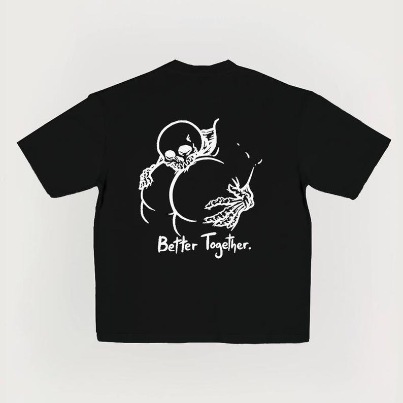 Puede incluir: Camiseta negra con un gr&aacute;fico blanco de un esqueleto abrazando dos formas redondeadas. El texto "Better Together" est&aacute; impreso debajo. La camiseta tiene mangas cortas y cuello redondo. El dise&ntilde;o es simple y audaz.