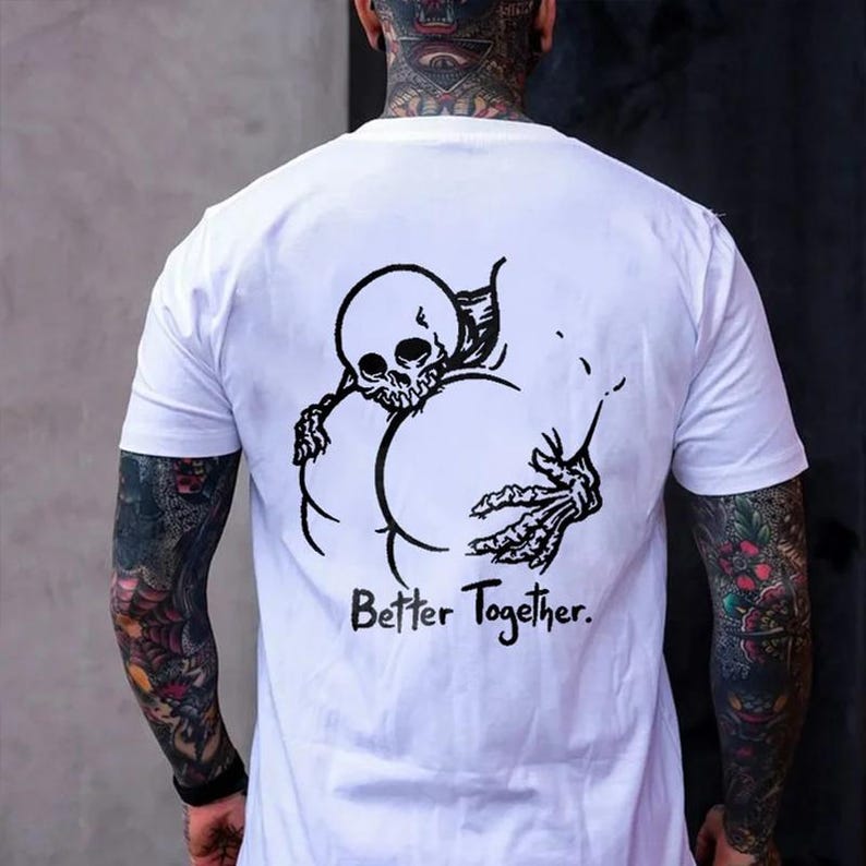 Puede incluir: Camiseta blanca con un gr&aacute;fico negro de un esqueleto abrazando una forma grande, con el texto "Better Together" debajo. El dise&ntilde;o est&aacute; centrado en la parte posterior de la camiseta. La persona que lleva la camiseta tiene tatuajes en los brazos y el cuello.