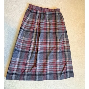 Puede incluir: Una falda a cuadros vintage en tonos grises, rojos y azules. La falda presenta un patrón de cuadros clásico con un diseño plisado. La falda está hecha de una tela suave y tejida y tiene una cintura alta.