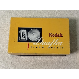 May include: A vintage Kodak Duaflex Flash Outfit box. The box is yellow with a black square containing a camera and flash. The Kodak logo and "Duaflex Flash Outfit" text are in red and white.