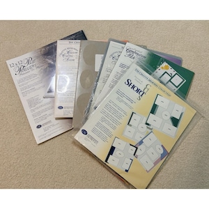 Puede incluir: Una colección de suministros de scrapbooking Creative Memories, que incluye protectores de páginas de 12x12, paquetes de sistemas de corte y paquetes combinados. Los artículos son de varios colores, con texto y gráficos visibles en el embalaje. Los productos están sobre una superficie clara.