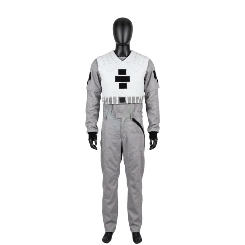 May include: A gray jumpsuit featuring a white chest plate with a black cross emblem and a white waist belt. The jumpsuit has long sleeves with black cuffs, a black patch on each shoulder, and a diagonal black zipper detail on the left hip area.