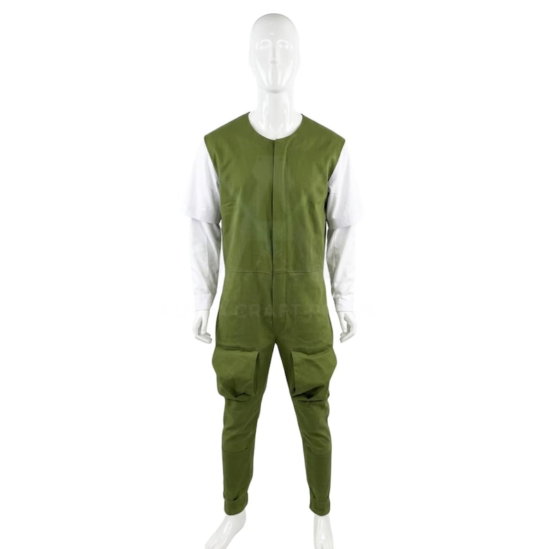 May include: A green jumpsuit with two front pockets and a white long-sleeved shirt underneath. The jumpsuit has a sleeveless design and a button-up front. The mannequin is standing against a white background.