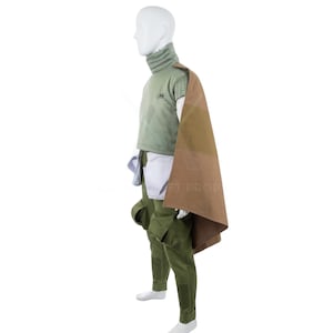 May include: A costume comprising a green turtleneck top, matching trousers, and a brown and tan cape. The outfit also features a white undershirt and a pouch. The costume is displayed on a mannequin.