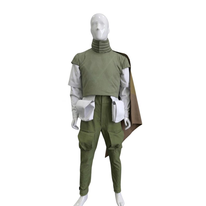 May include: A full costume displayed on a mannequin. The outfit comprises a green vest, trousers, and a cape. It also includes a white shirt, two white pouches, and a high-collared neck piece. The mannequin is set against a white backdrop.