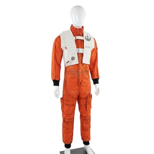 Può includere: Tuta arancione con gilet bianco, polsini neri e collo alto. Il gilet presenta un'emblema argentato e una fibbia. Il costume è esposto su un manichino. Questo è un costume da pilota di Star Wars.