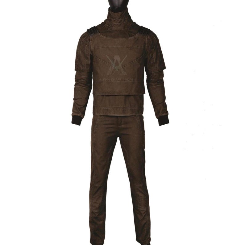 Puede incluir: Un conjunto de disfraz marr&oacute;n con una chaqueta de cuello alto con detalles en los hombros, una placa pectoral y pantalones a juego. La chaqueta tiene mangas largas con pu&ntilde;os negros. El disfraz tiene un aspecto texturizado y un logotipo en el pecho.