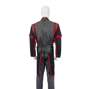 May include: A gray and black costume with red trim, displayed on a mannequin. The outfit includes a jacket with red accents, black sleeves, and matching pants. A black belt cinches the waist. The costume is designed for cosplay or themed events.