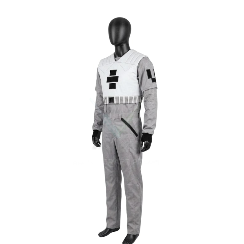 May include: A gray jumpsuit featuring a white chest vest with black rectangular accents, a V-neckline, and long sleeves. The jumpsuit includes a black diagonal pocket detail on the hip, a structured waist belt, and black wrist cuffs on a mannequin.