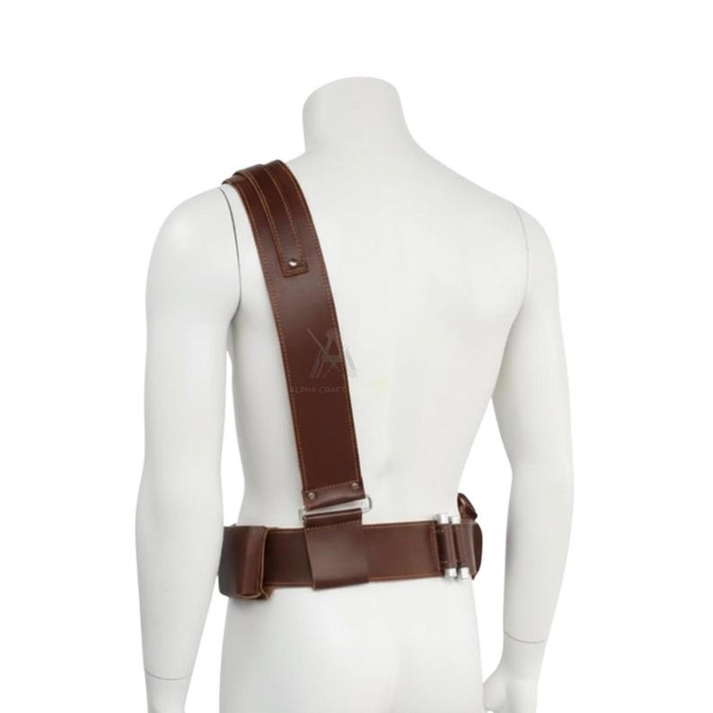 May include: A brown leather shoulder harness and belt set. The harness features a wide shoulder strap and a belt with a rectangular pouch and silver-toned hardware. The set is displayed on a white mannequin.