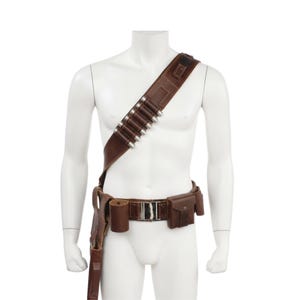 May include: Brown leather bandolier and belt set with silver bullet holders and a holster. The belt has a silver buckle and small pouches. The set is displayed on a white mannequin.