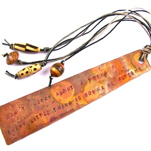 May include: Copper bookmark with the text "Don't worry about a thing, every little thing is gonna be alright". The bookmark has a rustic look and is decorated with wooden beads.