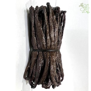 May include: A bunch of dark brown vanilla pods tied with black twine. The pods have a rich, oily appearance and are tightly bundled. The image is set against a white background.