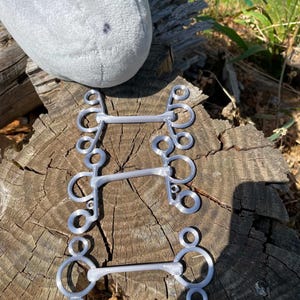 Peut inclure: Trois mors de cheval en métal argenté disposés verticalement. Chaque mors présente une embouchure droite reliée à des anneaux circulaires aux deux extrémités, avec des anneaux plus petits fixés aux composants circulaires principaux.