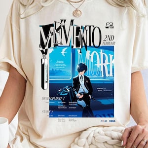 May include: Cream-colored t-shirt featuring a graphic design with the word "MEMENTO" in a bold, stylized font. The design includes an illustration of a person in a suit, with text that reads "2nd February" and "WORK".