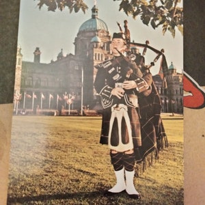 Regimental Piper do Regimento Escocês Canadense em frente aos edifícios do Parlamento - Victoria, B.C. - Cartão postal vintage