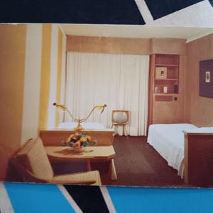 May include: Vintage photograph of a hotel room with two beds, a small television, and a table with a floral arrangement. The room has striped wallpaper and a built-in cabinet. The overall aesthetic is retro.