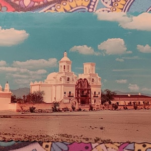 Pode incluir: Postal vintage com uma igreja branca em estilo missionário com duas torres sineiras e uma fachada detalhada. A igreja está situada contra um céu azul com nuvens brancas fofas. O primeiro plano mostra uma paisagem desértica.