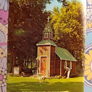 May include: A small, wooden chapel with a cross on top, surrounded by green trees and grass. The chapel has a green roof and a brown door. The text "THE LITTLE CHAPEL OF THE FLOWERS" is written below the image. The text "Located at Schroeder's Floral, Eagle Bend, Minnesota 56446" is written below the chapel.