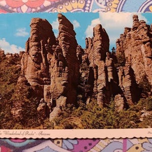 Pode incluir: Postal vintage com uma vista panorâmica de formações rochosas sob um céu azul com nuvens. O postal é intitulado "The Wonderland of Rocks - Arizona" e tem uma borda ondulada. A foto é de Mae Miller.