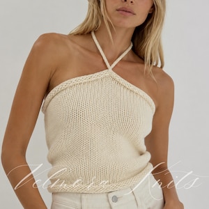 Könnte beinhalten: Ein cremefarbenes Strick-Neckholder-Top mit einem dicken geflochtenen Nackenband und einem einfachen glatten Rechts-Strickmuster. Das Kleidungsstück hat ein schlichtes ärmelloses Design mit geradem Saum und dem Wasserzeichen Velmora Knits.