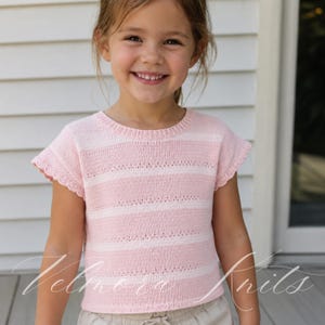 May include: A pink and white striped knit top with short sleeves. The top has a round neckline and a scalloped edge on the sleeves. The image shows a young girl wearing the top.