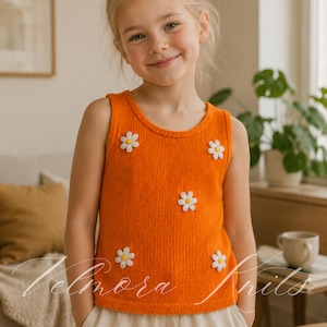 May include: An orange knitted tank top adorned with white daisy appliqués. The sleeveless top features a round neckline and is made of a textured knit fabric. The top is a bright, cheerful color and is suitable for children.