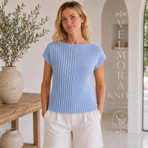 Puede incluir: Una blusa de punto de manga corta en color azul claro con textura acanalada vertical en el lado izquierdo y textura de punto liso en el derecho, con cuello ancho y dobladillo acanalado. El texto VELMORA KNITS KNITTING PATTERNS es visible a la derecha.