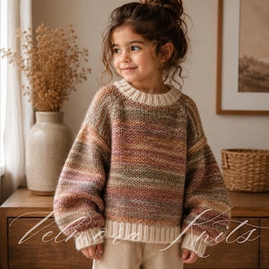 May include: A child wearing a multi-colored knit sweater with a cream-colored neckline and cuffs. The sweater features horizontal stripes in shades of brown, pink, green, and yellow. The child is smiling and wearing beige pants.
