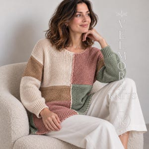 May include: A long-sleeved, colour-blocked knit jumper featuring panels of cream, tan, dusty rose, and sage green. The garment has a round neckline and ribbed cuffs. Text on the right side reads VELMORA KNITS with a circular logo below.
