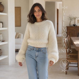 Peut inclure: Un pull en tricot duveteux de couleur crème à manches longues, col rond et poignets côtelés, porté avec un jean en denim bleu clair. L'image contient le texte vertical VELMORA KNITS KNITTING PATTERNS avec un logo circulaire.