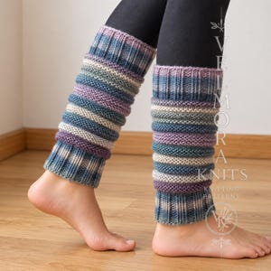 Könnte beinhalten: Ein Paar gestrickte Stulpen mit horizontalen Streifen in Blau-, Lila- und Cremetönen. Die Stulpen haben eine gerippte Textur an den oberen und unteren Rändern und ein kraus rechts gestricktes Muster in der Mitte, das die Unterschenkel bedeckt.