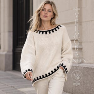 Può includere: Un maglione in maglia a maniche lunghe color bianco sporco con un motivo geometrico nero lungo l'ampio scollo e i polsini. Il testo VELMORA KNITS KNITTING PATTERNS è visibile sul lato destro dell'immagine in una disposizione verticale e orizzontale.