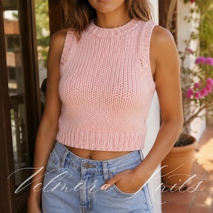 May include: A light pink, sleeveless, knitted crop top with a ribbed hem and neckline. The top is made of a soft, textured yarn and is paired with blue jeans. The brand name "Velmora Knits" is visible in the image.