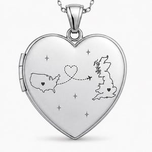 May include: Two heart-shaped lockets on chains, one gold-toned and one silver-toned. Each locket features an engraved map of the United States and the United Kingdom connected by a dashed flight path with a small airplane and heart icons.