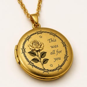 Può includere: Un ciondolo a medaglione circolare color oro su una catenina abbinata. Il fronte presenta una rosa incisa, due piccole stelle e un bordo di filo spinato che circonda il testo "This was all for you" in un carattere serif scuro e chiaro.