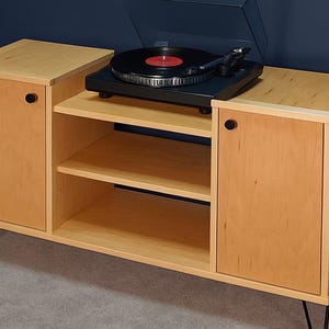 May include: A light wood record player console with a black turntable and red record. The cabinet has two doors with black knobs, two shelves, and black hairpin legs. The cabinet is approximately 48 inches wide.