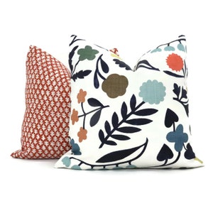 May include: Two decorative throw pillows, one with a red and white geometric pattern and the other with a white background and a colorful floral pattern featuring blue, green, orange, and brown.