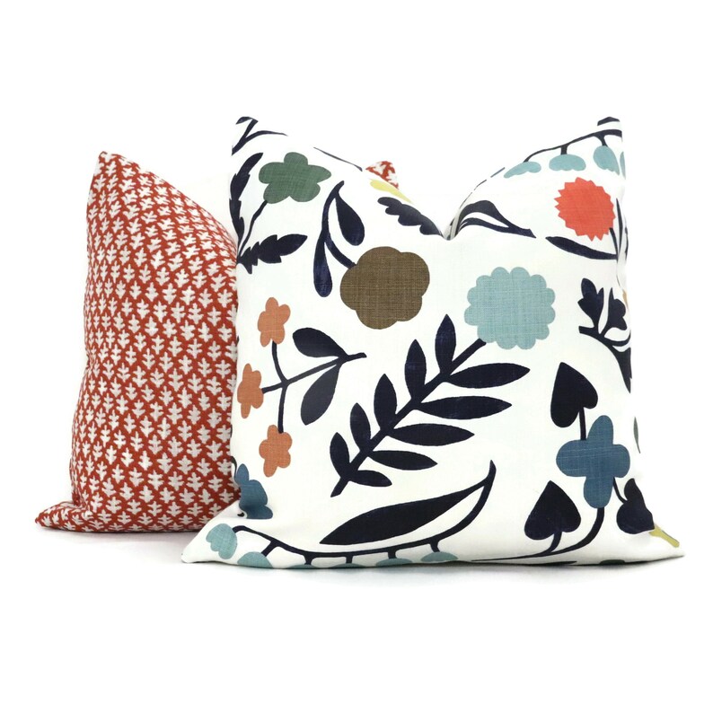 May include: Two decorative throw pillows, one with a red and white geometric pattern and the other with a white background and a colorful floral pattern featuring blue, green, orange, and brown.
