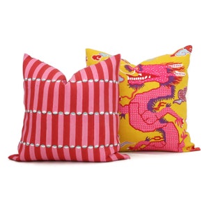 May include: Two decorative throw pillows. One pillow has a red and white striped pattern with a row of white circles. The other pillow has a yellow background with a pink dragon design.