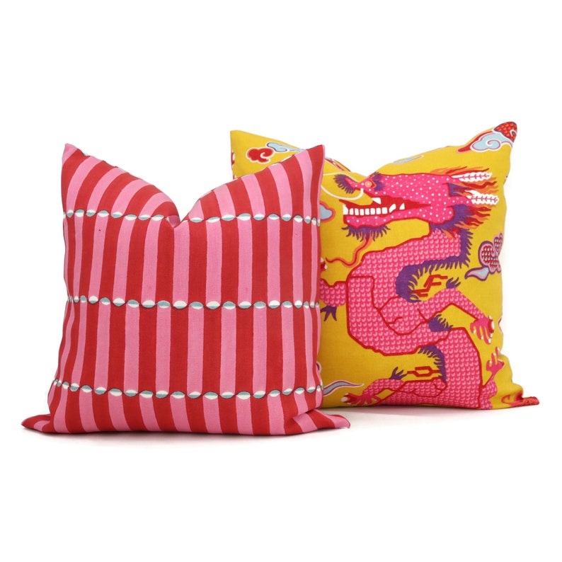 May include: Two decorative throw pillows. One pillow has a red and white striped pattern with a row of white circles. The other pillow has a yellow background with a pink dragon design.