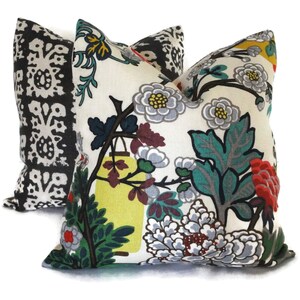 May include: Two decorative throw pillows. One pillow features a black and white floral pattern. The other pillow has a cream background with a colorful floral design, including gray, red, yellow, and green elements. The pillows are square-shaped.