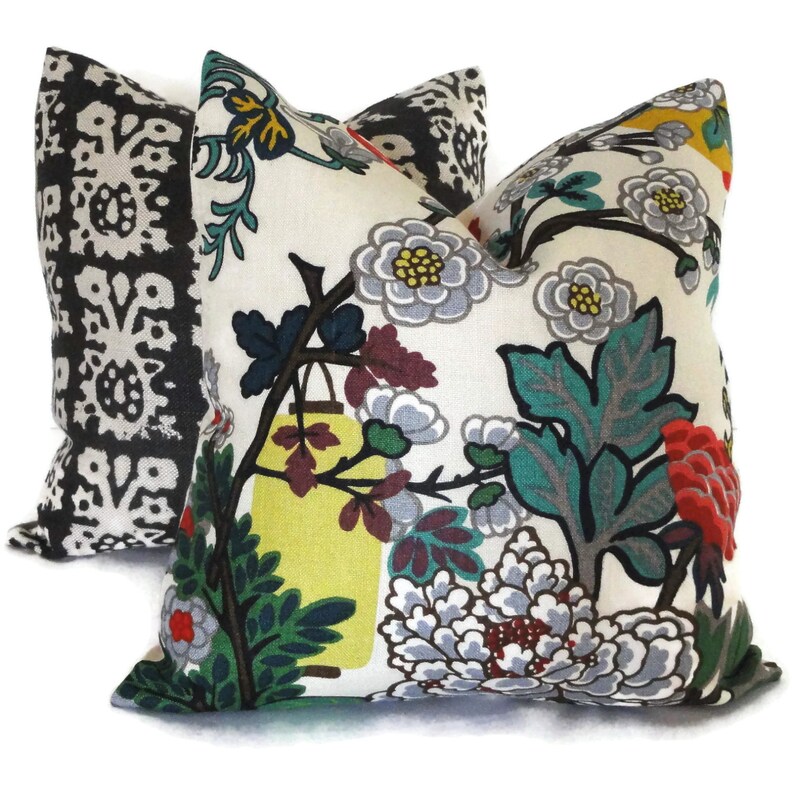 May include: Two decorative throw pillows. One pillow features a black and white floral pattern. The other pillow has a cream background with a colorful floral design, including gray, red, yellow, and green elements. The pillows are square-shaped.
