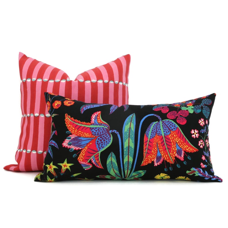 May include: Two decorative throw pillows. One pillow is red and white striped with a white polka dot pattern. The other pillow is black with a colourful floral pattern featuring red, orange, yellow, green, and blue flowers.