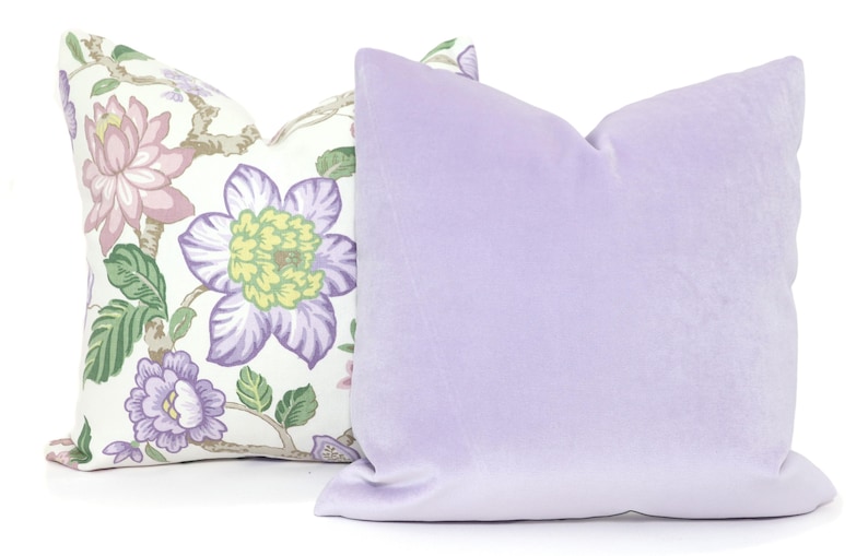 May include: Two decorative throw pillows, one with a floral pattern in shades of pink, green, and purple on a white background, and the other a solid lavender colour.