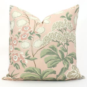 May include: A decorative pillow with a floral pattern. The pillow features a light pink background with a repeating design of flowers, leaves, and other botanical elements in shades of pink, green, and cream. The pillow is square-shaped.