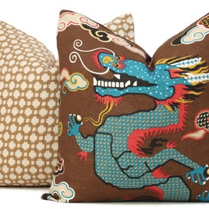 May include: Two decorative throw pillows with a brown background. One pillow features a repeating geometric pattern in white and brown. The other pillow features a colourful dragon design with clouds and a red, blue and yellow colour scheme.
