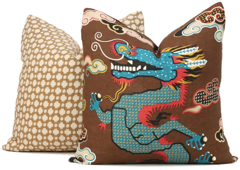 May include: Two decorative throw pillows with a brown background. One pillow features a repeating geometric pattern in white and brown. The other pillow features a colourful dragon design with clouds and a red, blue and yellow colour scheme.