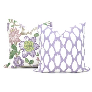 May include: Two decorative throw pillows, one with a floral pattern in shades of purple, green, and pink on a white background, and the other with a white and lavender geometric pattern.