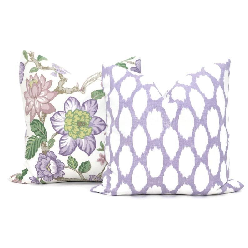 May include: Two decorative throw pillows, one with a floral pattern in shades of purple, green, and pink on a white background, and the other with a white and lavender geometric pattern.